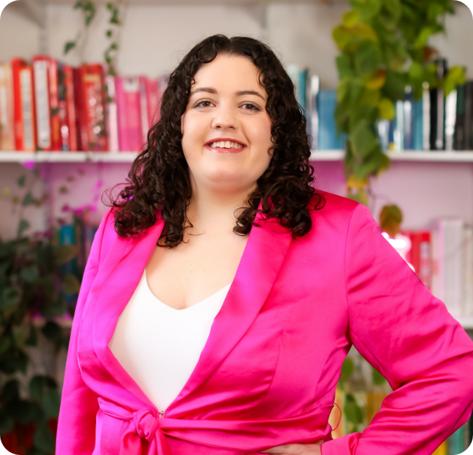 Portrait of the founder of YorkPoint Digital, wearing a bright pink blazer and smiling confidently in a vibrant office setting with books and greenery in the background.