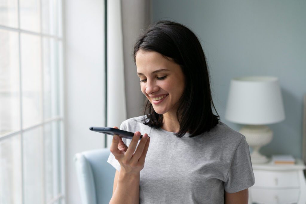 A smiling woman using voice search on her smartphone in a bright room, illustrating the growing trend of voice search for local businesses.
