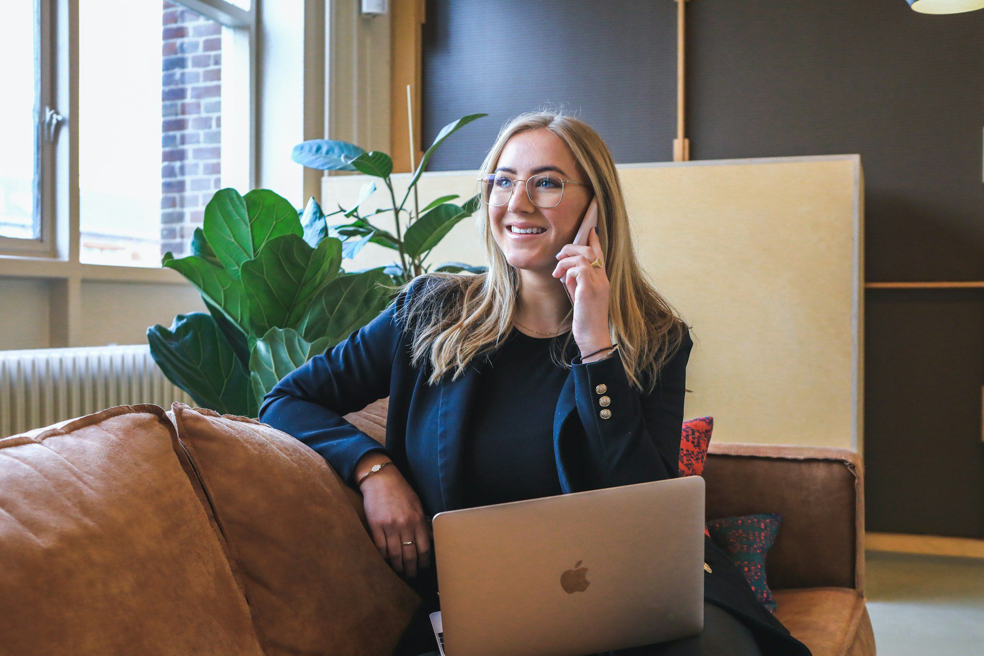 Smiling businesswoman talking on the phone with a laptop open, discussing a website redesign project in a modern office setting.