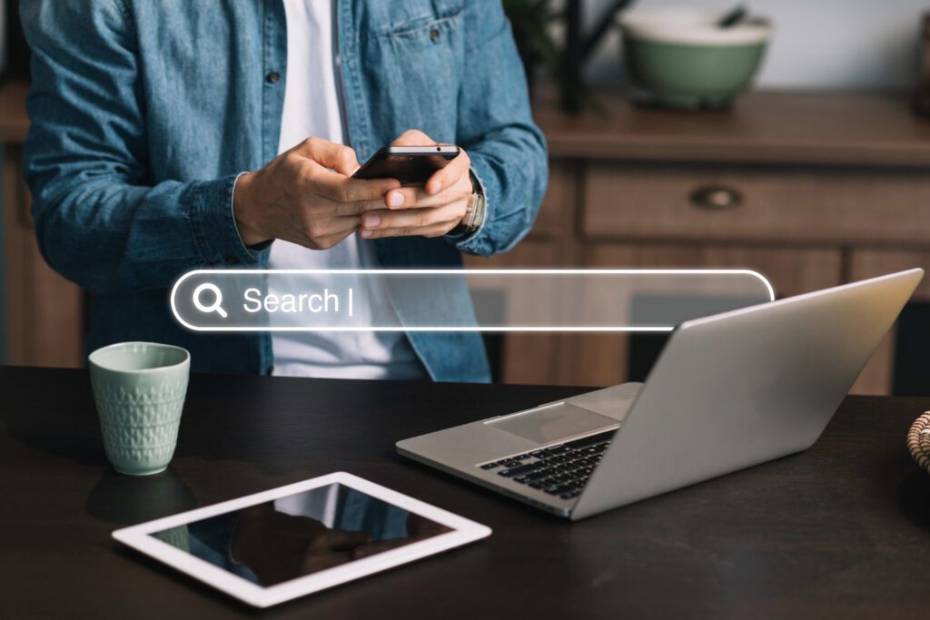 Man using smartphone and laptop with search bar overlay, symbolizing long-tail keyword research for SEO.